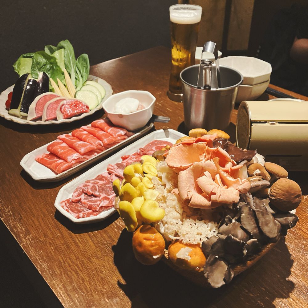 きのこの盛り合わせが乗ったカゴと、鍋用の肉と野菜が盛られた皿の写真