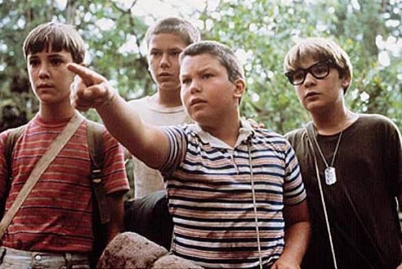 Still shot from the movie Stand By Me showing four young teens standing together, with one pointing ahead. 