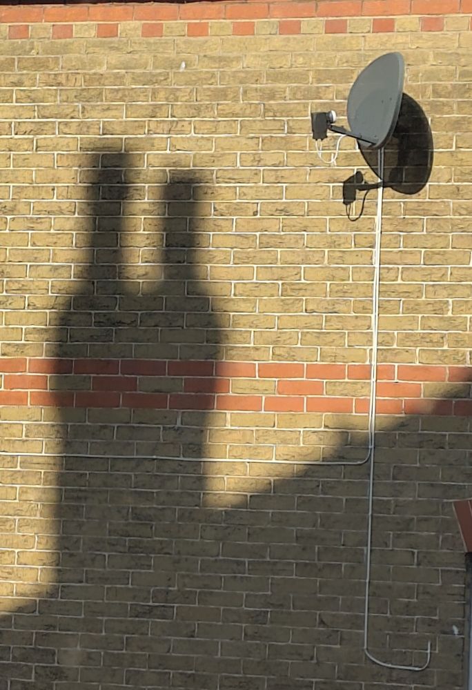 A yellow brick wall with a satellite dish top right.

The lower half of the wall is in shadow of a sloping roof, and on the left is a chimney stack with 2 pots at the top - that overall sort of a bit looks like 2 people stood uncomfortably close together 