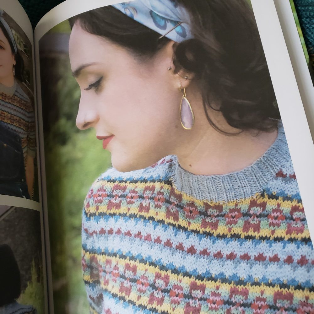 Detail of a pullover with bands of stranded colorwork in blues, yellows, and pinks. 