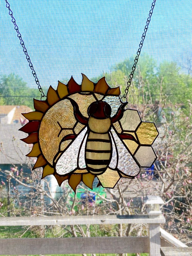 A stained glass suncatcher of a sunflower, bee, and honeycomb.