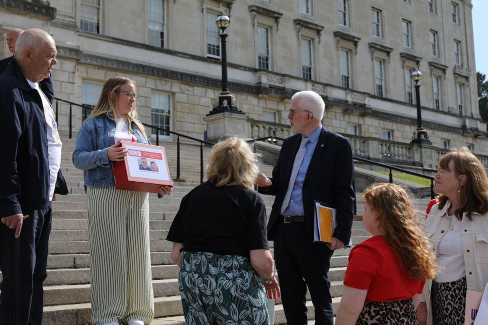 Stewart Dickson MLA standing on Stormont steps holding the petition, talking to Isla Gear and her family.