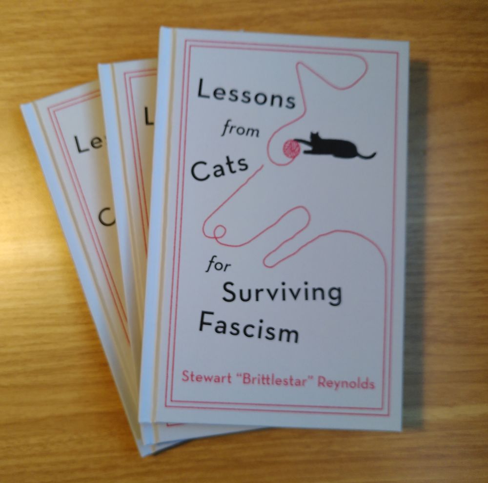 Three books on my desk, all of them "lessons from cats for surviving fascism" by Stewart "brittlestar" Reynolds.
Coverart: a black cat playing with a ball of red yarn, part of which unraveled to form a dog with the remaining ball of yarn representing the eye. 