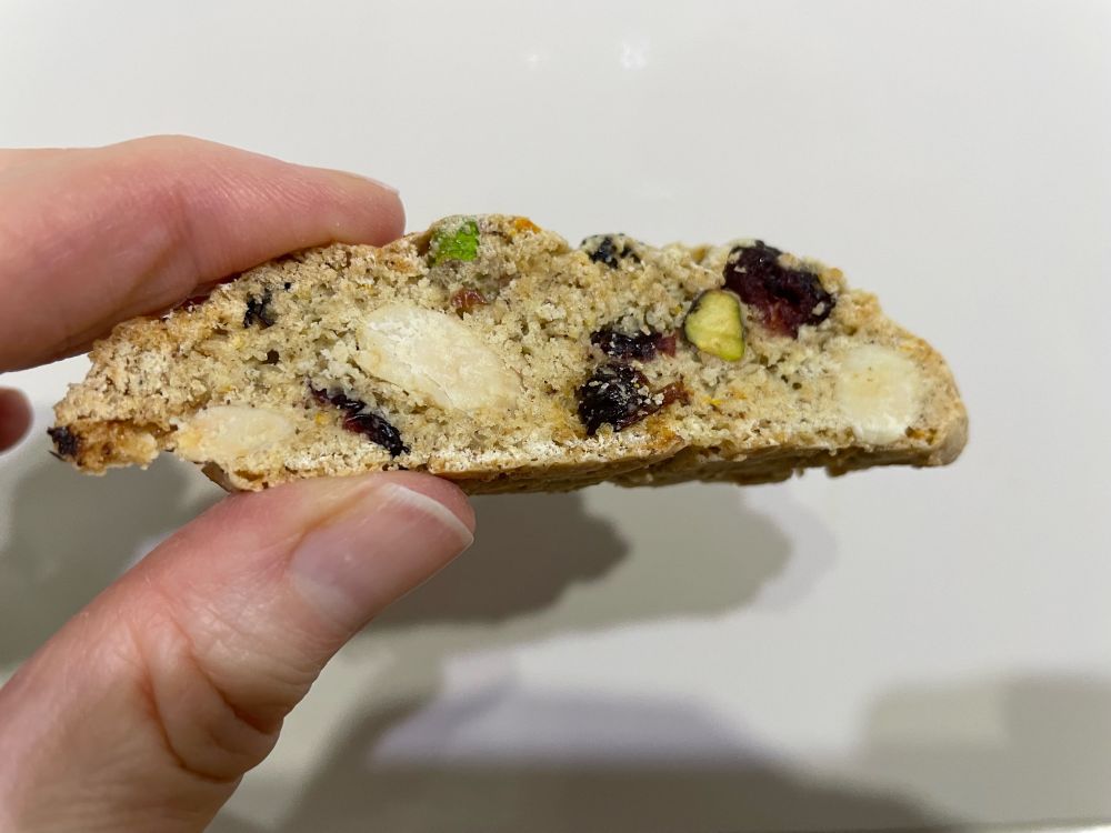 Thumb and finger holding a biscuit full of dried fruit and nuts