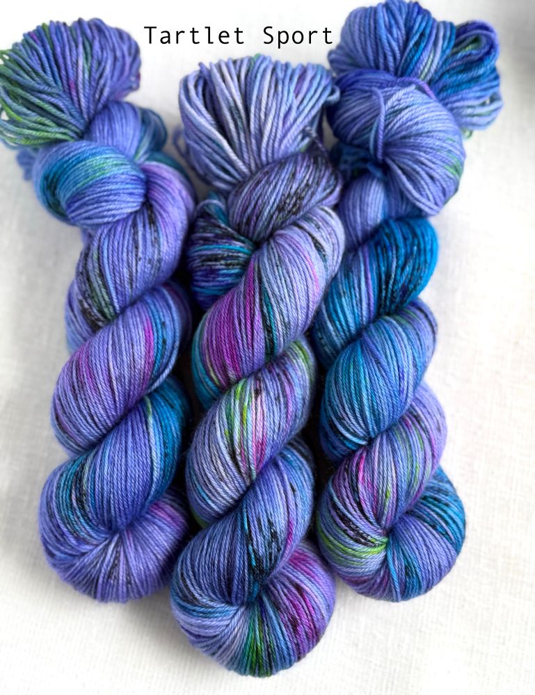 Three skeins of yarn side by side on a white background. The yarn is bright purple background with splashes of black, hot pink, chartreuse green, purple, turquoise. 