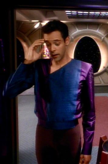 cropped screencap from star trek: deep space nine S3E10 “fascination”: julian bashir experiencing a headache from zanthi fever, a telepathic disease he was just infected with. 

he’s wearing civilian clothes—red trousers, plus a silky long-sleeved shirt with shoulder pads and an elasticized waist. the shirt collar is an asymmetrical triangle that dips temptingly below his collarbone on one side. the shirt is made of wide alternating vertical stripes of plain purple shiny fabric and shiny dark blue fabric with a grid pattern. the right sleeve and shoulder is 100% blue fabric while the left sleeve and shoulder is 100% purple.
