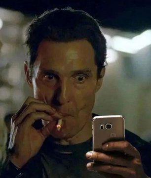 matthew mcconaughey taking a drag of a cigarette as he stares at his phone, distressed