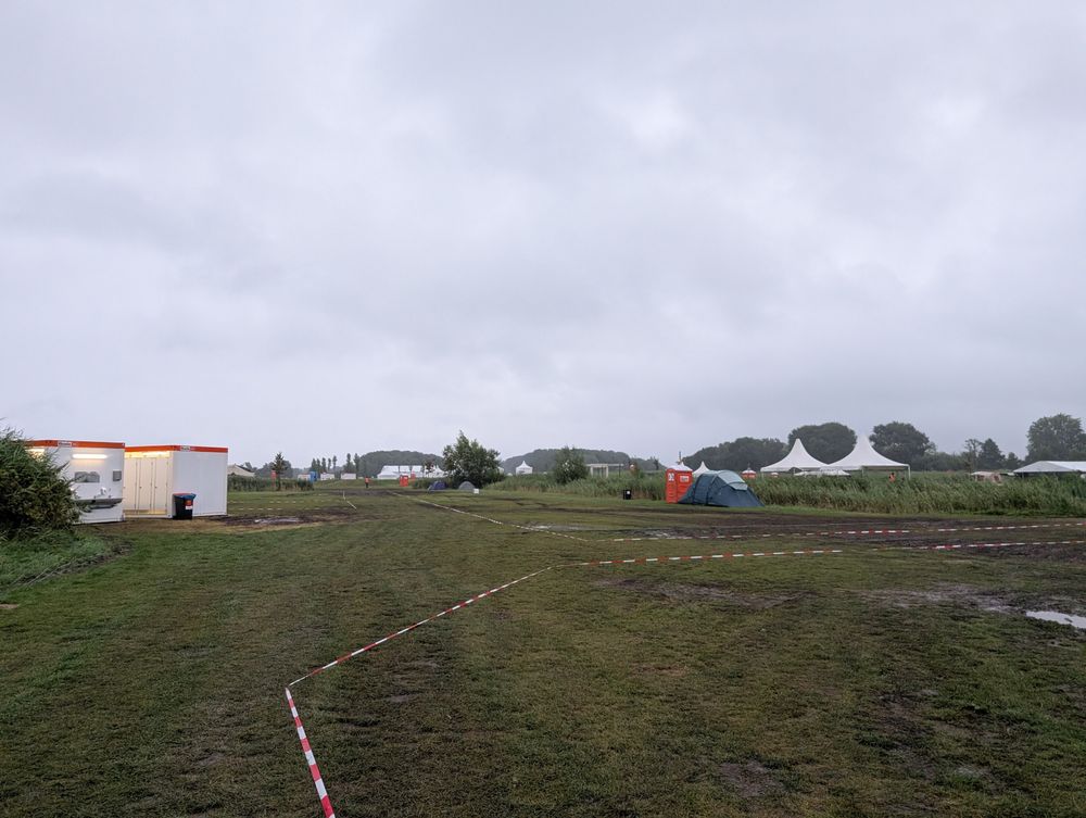 A muddy field with tents in the background, and barrier tape. It's raining and muddy 