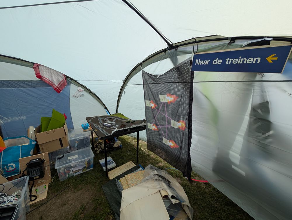 A model railway in the corner of the tent. A ServFail flag hangs next to an NS "naar de trainen" sign