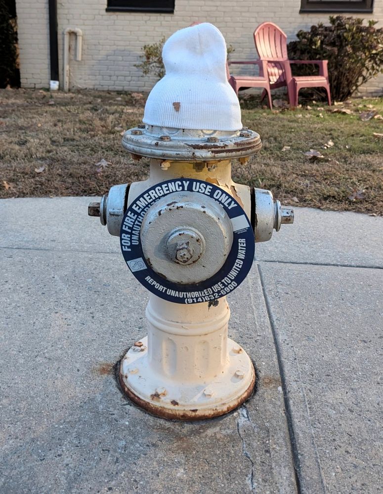 A yellow fire hydrant with a white beanie on top 
