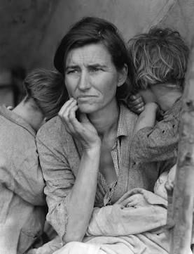 Woman sits in doorway with her two children who have their heads turned away from the camera. They appear poor and malnourished.