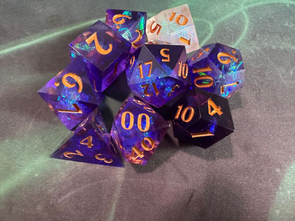 A closeup photo of Daggerheart’s purple polyhedral dice set, with two uncommonly shaped d12s in mother-of-pearl and twilight purple. 