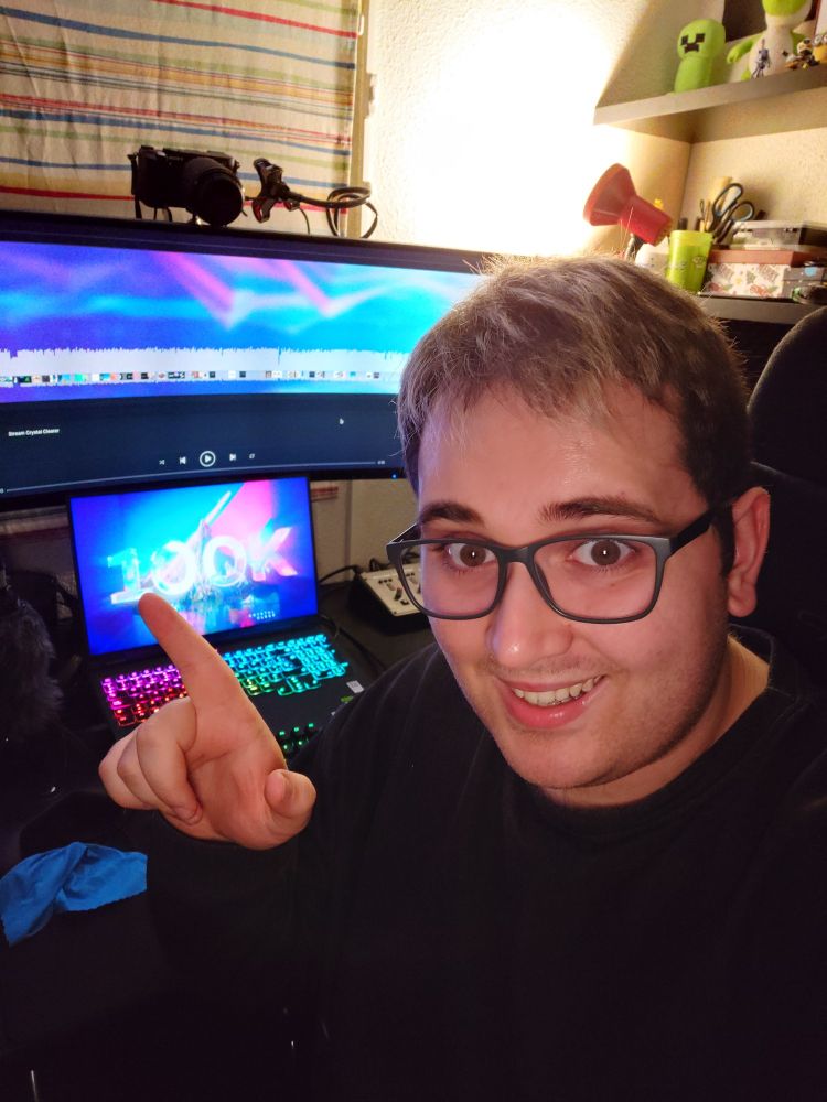 modus celebrates a recent milestone: reaching 100,000 plays on his song 'Crystal Clear'. He's looking at the camera while pointing at the screens in his studio, which show images of the achievement.