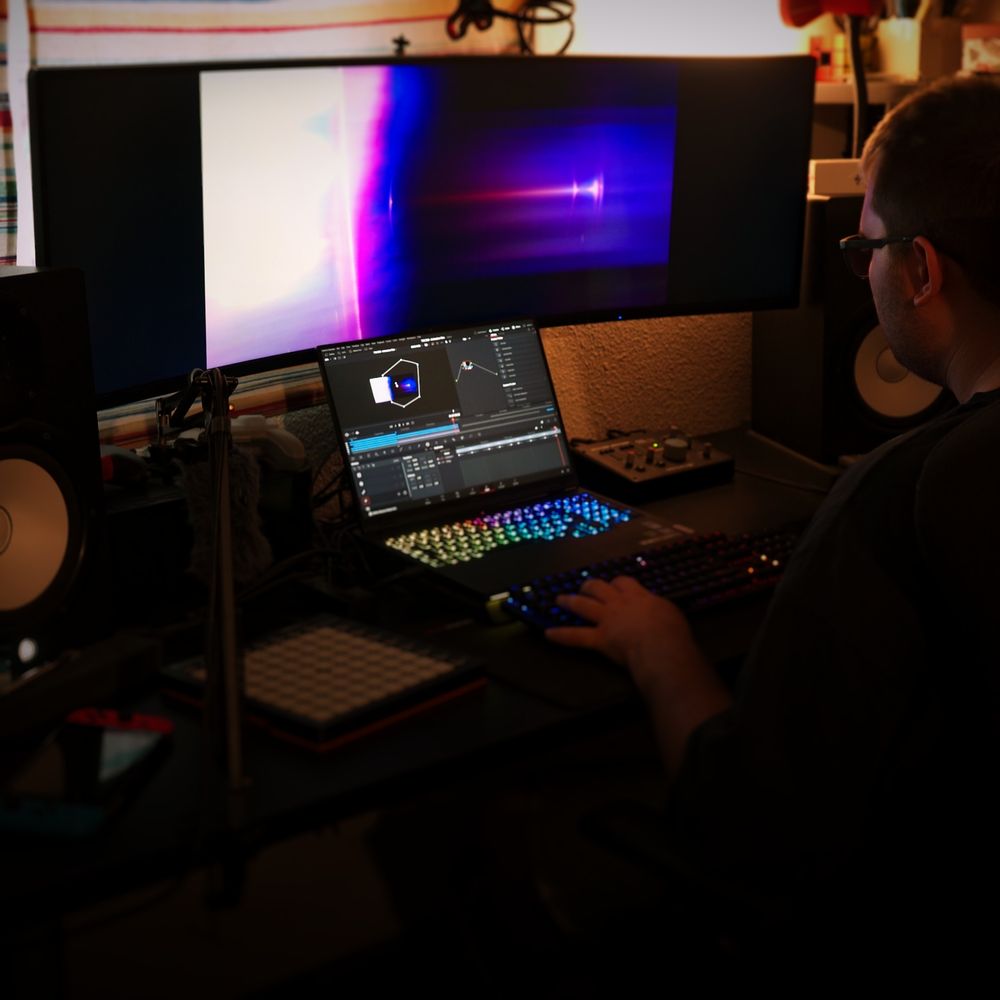 modus is seen in his studio working on the animation film for 'New Year Protocol X: The End'. He is sitting down, with one hand on his keyboard and the other on his mouse, as he works on the visual effects for the film.