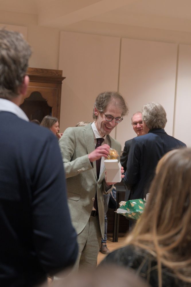Ik sta middenin een groep mensen, breed glimlachend. Uit een kubusvormig doosje haal ik een gouden kerstbal.