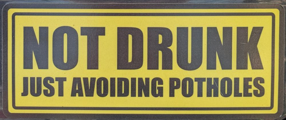Sticker on the back of a car with text "NOT DRUNK, Just avoiding potholes"