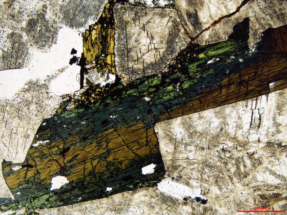 A rock thin section showing an interstitial space between feldspar crystals which change in colour from brown to blue to green as the mineralogy changes.