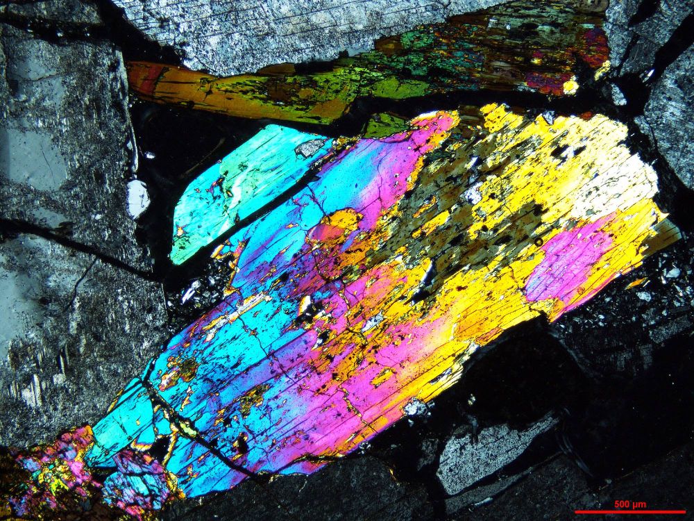 An image of a rock under the microscope. A large crystal of brightly coloured aegirine surrounded by alkali feldspar crystals.