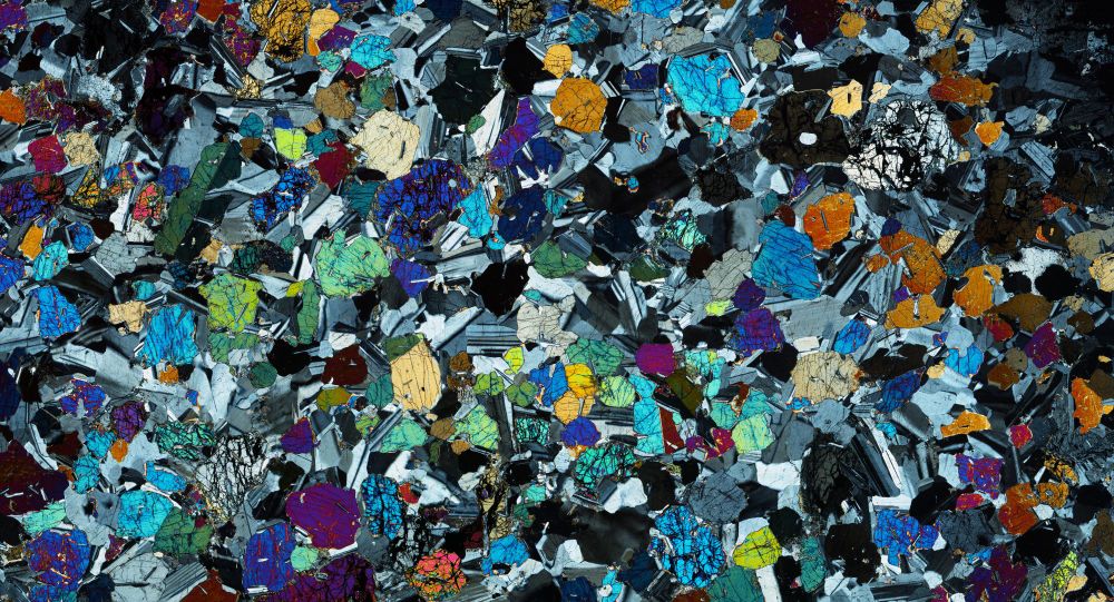 An image of a rock thin section viewed under the microscope in cross-polarised light. Three minerals (olivine, clinopyroxene, and plagioclase feldspar) are visible.