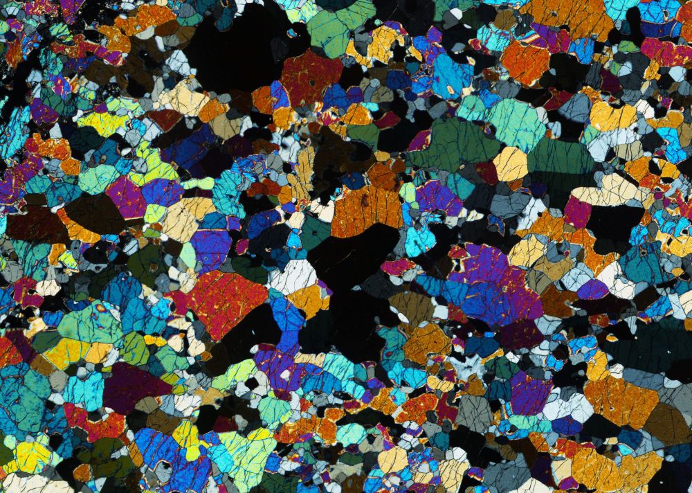 An image of a rock thin section under the microscope showing an array of brightly coloured crystals of the mineral olivine.
