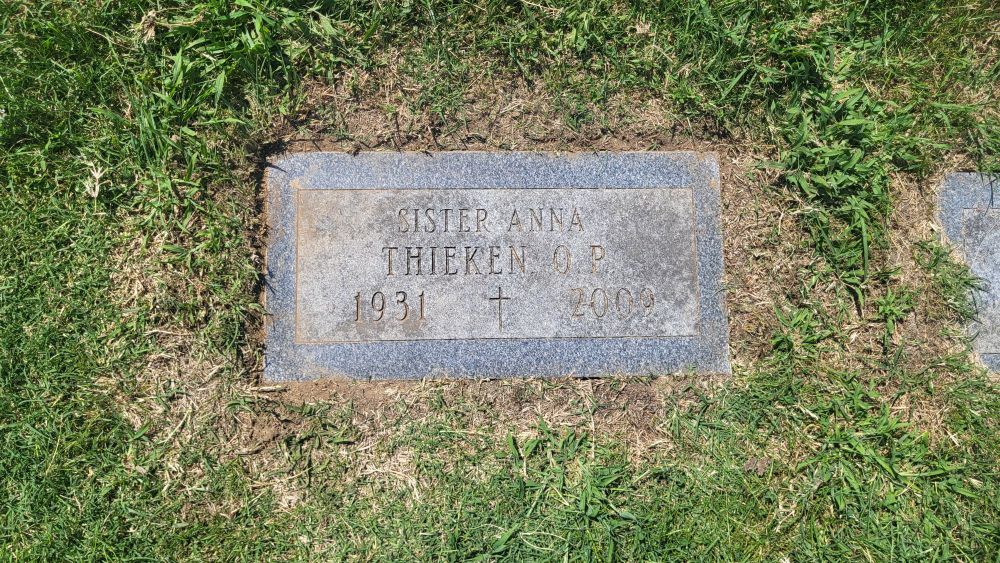 A flat slightly over grown headstone sinks into the earth. Sister Anna Thieken O.P. 1931 - 2009. At the edge of the picture another headstone is sinking further into the dirt. 