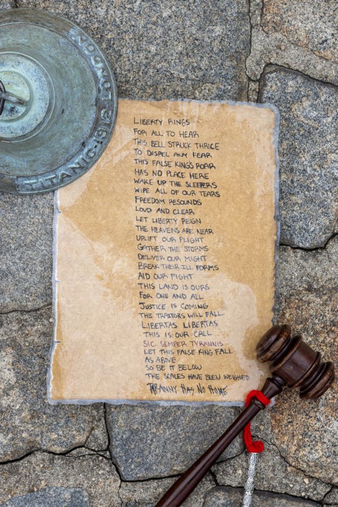The bell and the hammer to ring it weigh down a piece of paper with the following poem written on it:

"Liberty rings
For all to hear
This bell struck thrice
To dispel any fear
This false king's roar
Has no place here
Wake up the sleepers
Wipe all of our tears
Freedom resounds
Loud and clear
Let liberty reign
The heavens are near
Uplift our plight
Gather the storms
Deliver our might
Break their ill forms
Aid our fight
This land is ours
For one and all
Justice is coming
The traitors will fall
Libertas Libertas
This is our call
Sic Semper Tyrannis
Let this false king fall
As above
So be it below
The scales have been weighed
Tyranny has no throne"