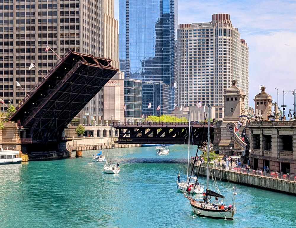 Photo of a raised bridge over the Chicago river with 5 sailboats floating under it
