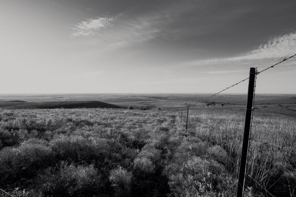 A digital black and white photo of the flint hills with a barbed wire fence running down the right side of the photo. 