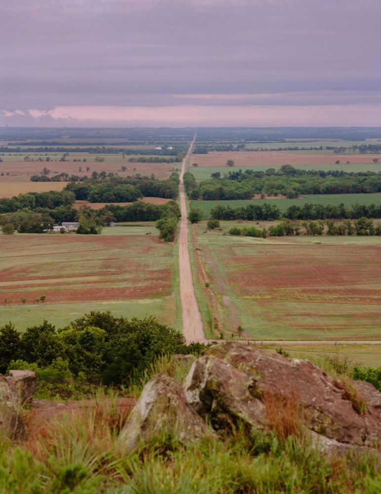 A medium format film photo of a long road leading out of a large hill into the horizon. 