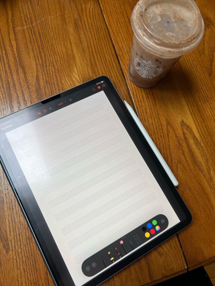 Picture of my iPad displaying a blank “sheet of staff paper” in the MusicPad app. The Apple Pencil is attached to the side of the iPad and there is a Starbucks beverage in the top right corner of the picture. 