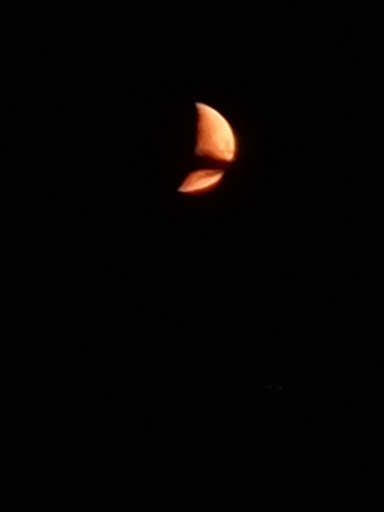 Orange crescent moon with a black shadow of a cloud cutting across the middle and surrounded by black sky