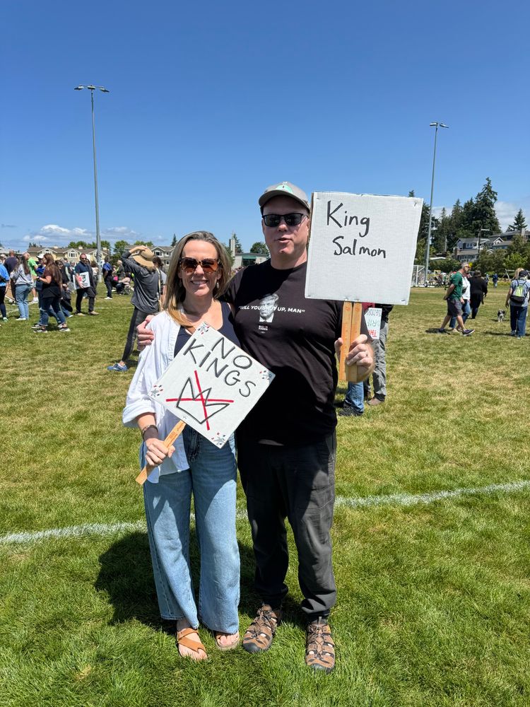 Me and my husband standing in the park at the protest with our No Kings signs. 