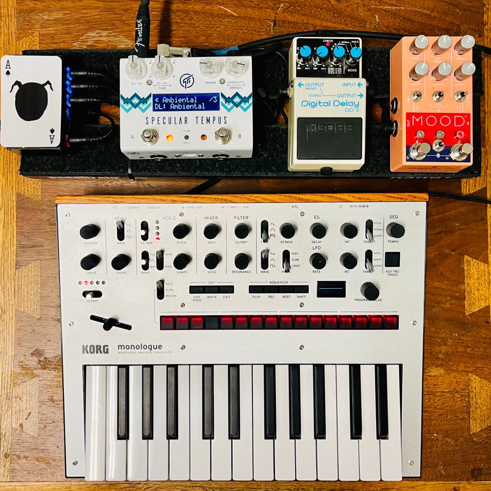 A silver Korg Monologue analog synth sitting on a table connected to pedals: Specular Tempus set on an ambient patch, a Boss DD-2 and a Chase Bliss Mood mk1.
