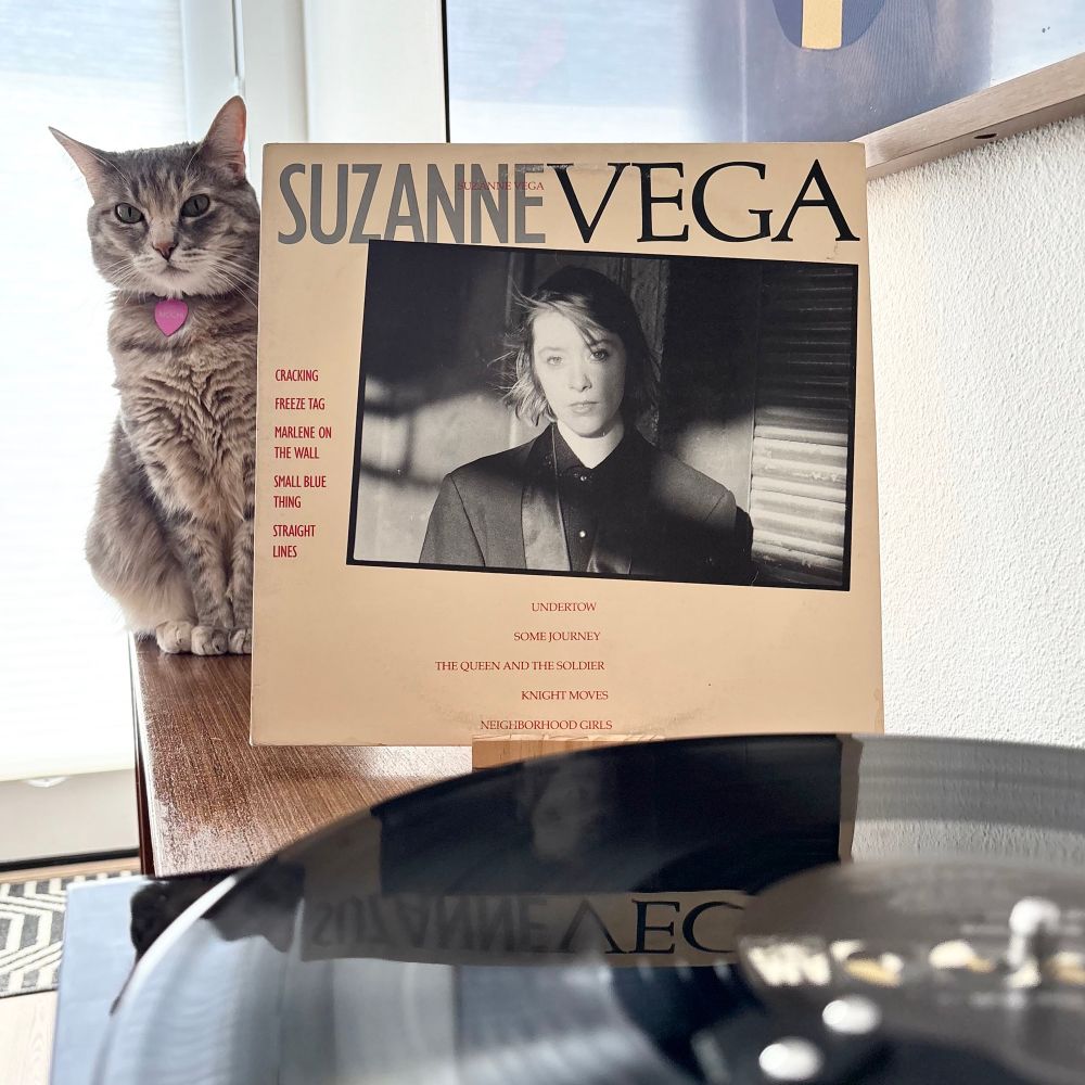 Torbie cat sitting next to record jacket of Suzanne Vega’s self titled debut. Record spinning in the foreground.