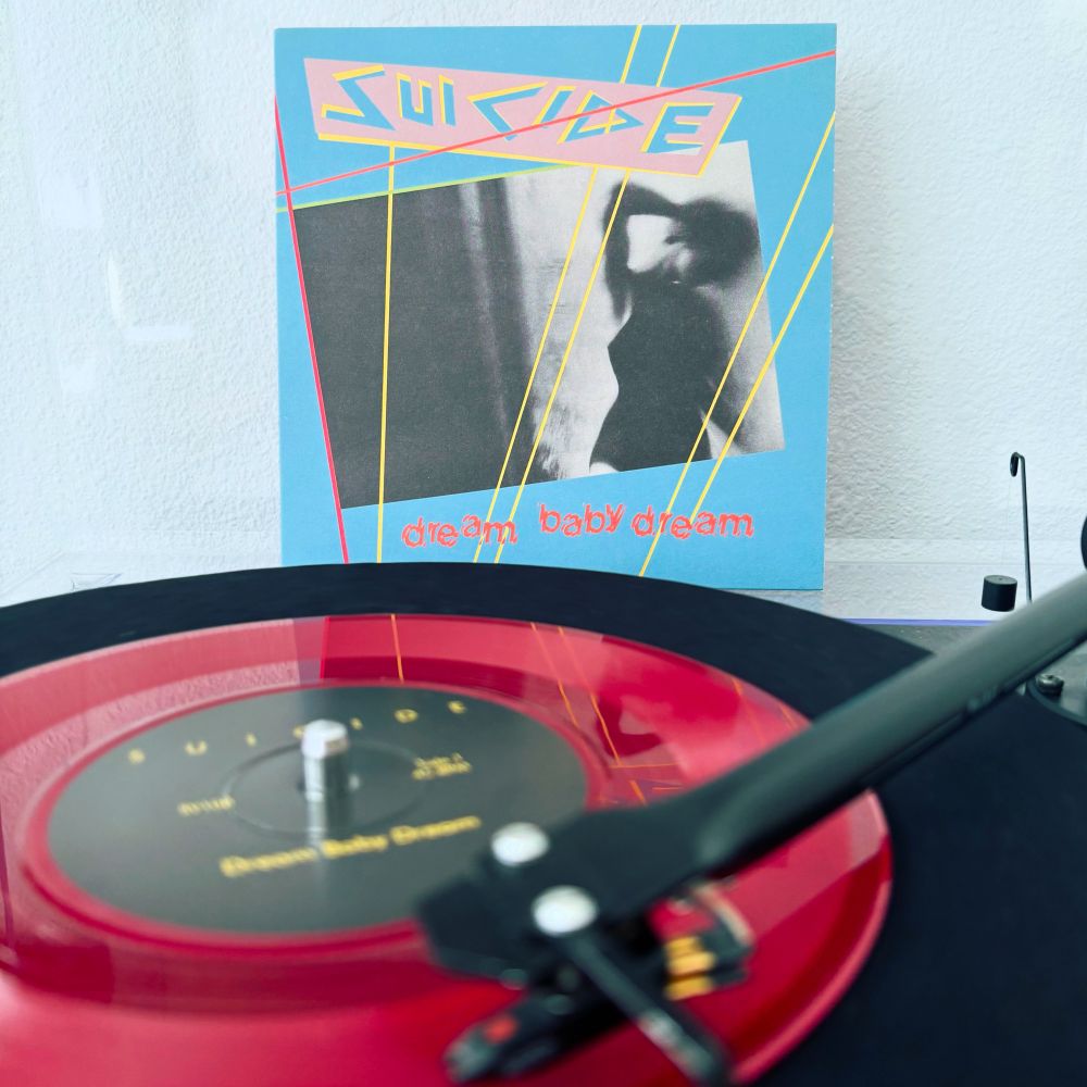 Red vinyl 7” single spinning of Suicide’s Dream Baby Dream. Sleeve displayed in the background.