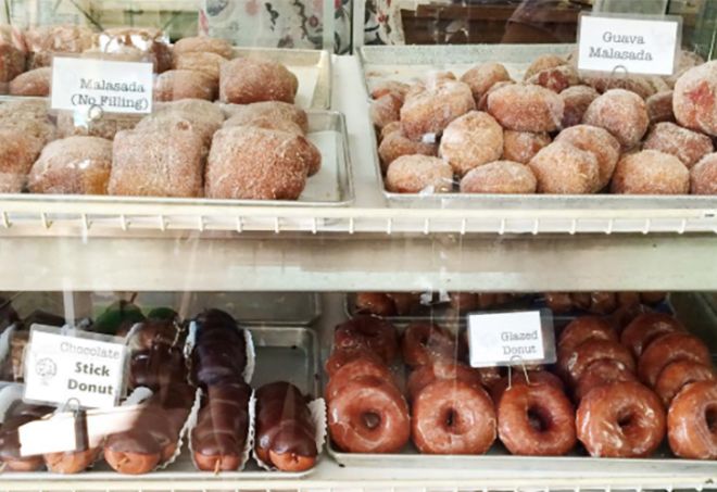 Photo of a bakery case filled with malasadas and donuts. 