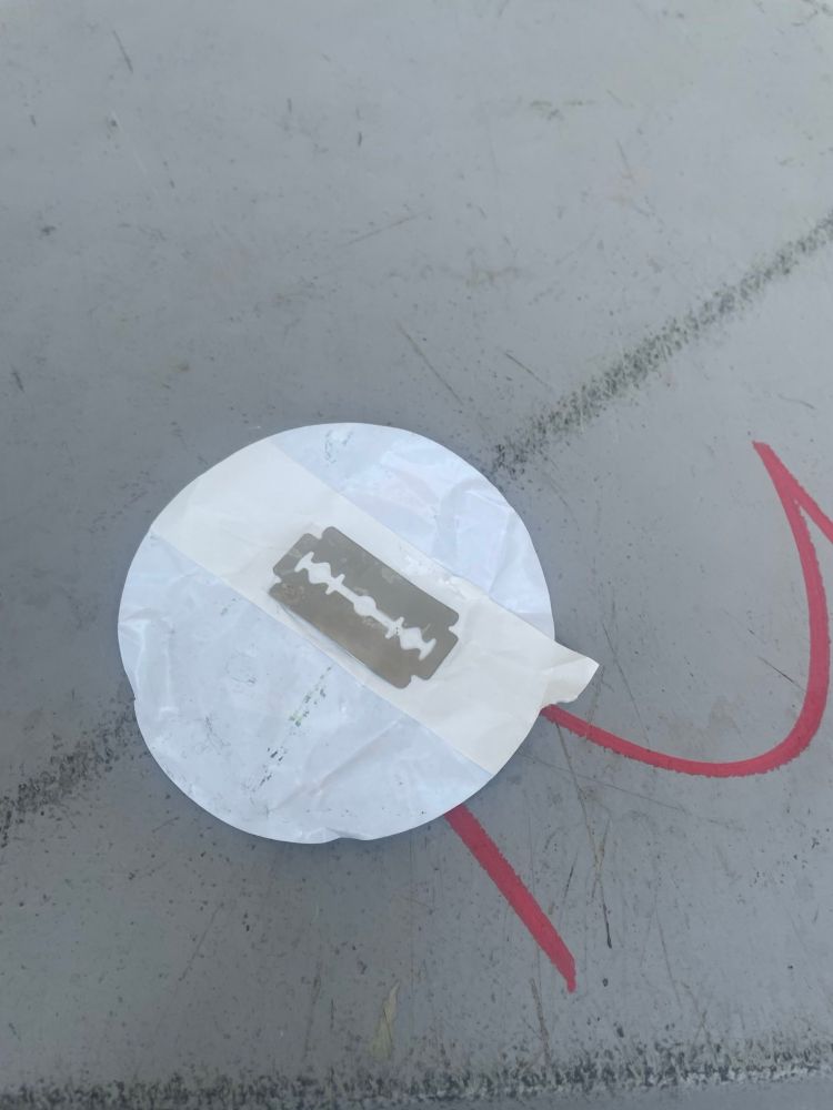 Unter dem AfD-Sticker klebt eine Rasierklinge auf einem Klebeband.