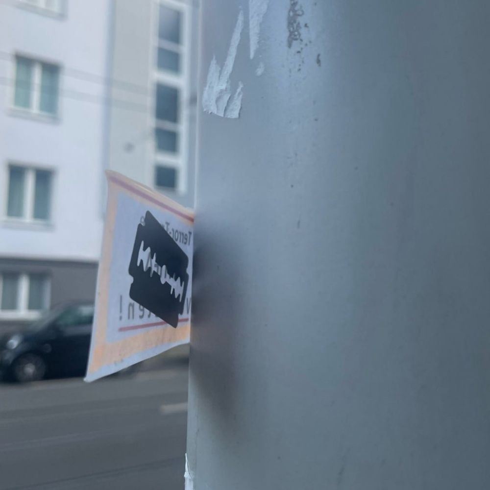 Foto zeigt halb entfernten Sticker mit der Aufschrift „Terror-Truppe Antifa Verbieten!“.
Eine Rasierklinge ist an der Unterseite des Stickers zu erkennen.