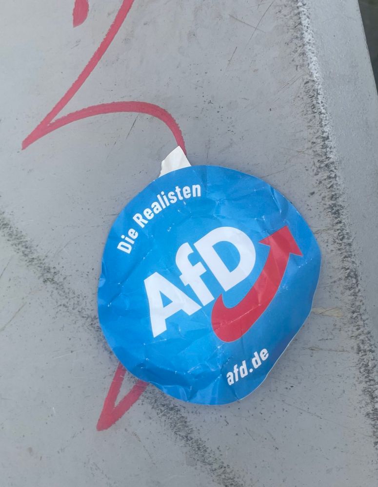 Ein AfD-Sticker mit Logo der extrem rechten Partei und der Aufschrift „Die Realisten“ klebt an einem Gegenstand.