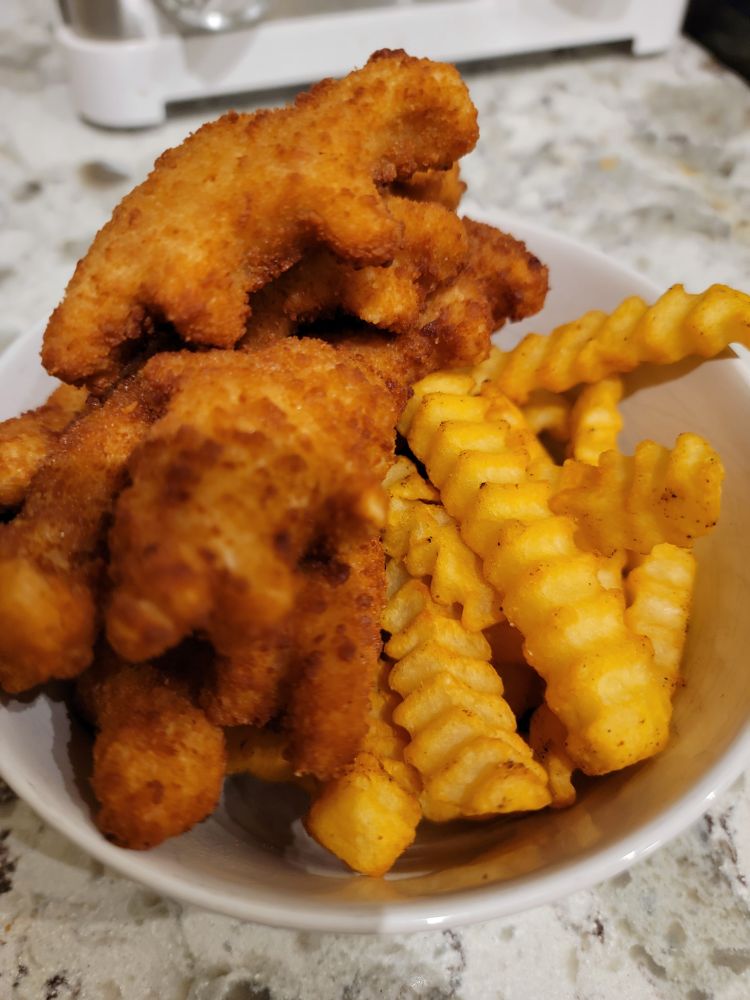 A bowl of dinosaur shaped nuggets and crinkle cut fries.