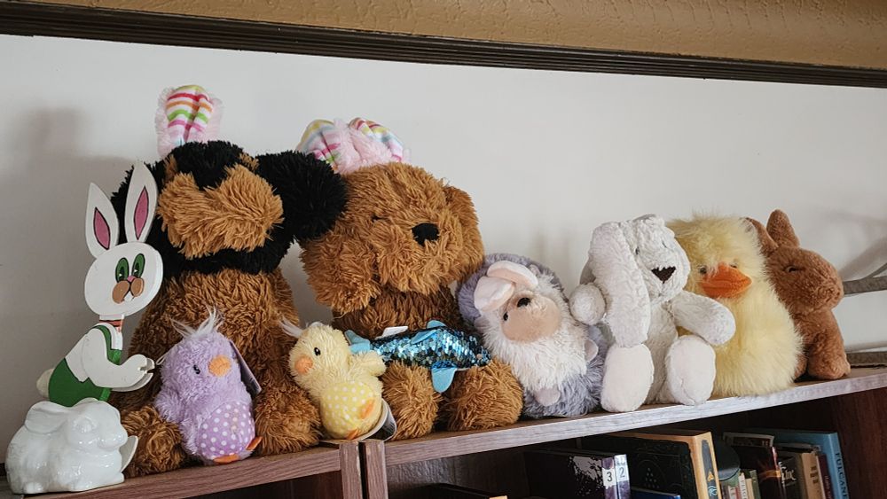 Easter plush toys and a balsawood bunny MFM painted, in a row atop by bookshelf