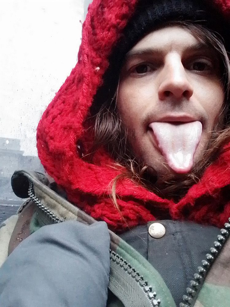 Miu in carhartt bibs an army jacket and red scarf doing colon P emoji in real life