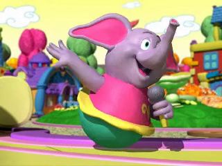 Tibby Wobnobbin (lavender elephant with no legs wearing a pink dress with yellow tutu and a teal bottom) holds a microphone while attempting to vibrate mud off the shipping label of a package.