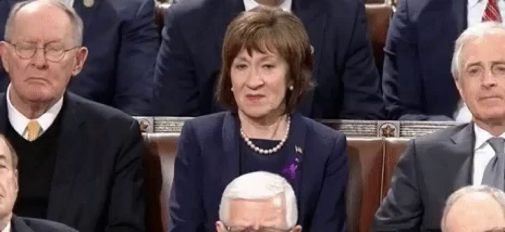 a woman in a pearl necklace is sitting in a row of men in suits and ties .