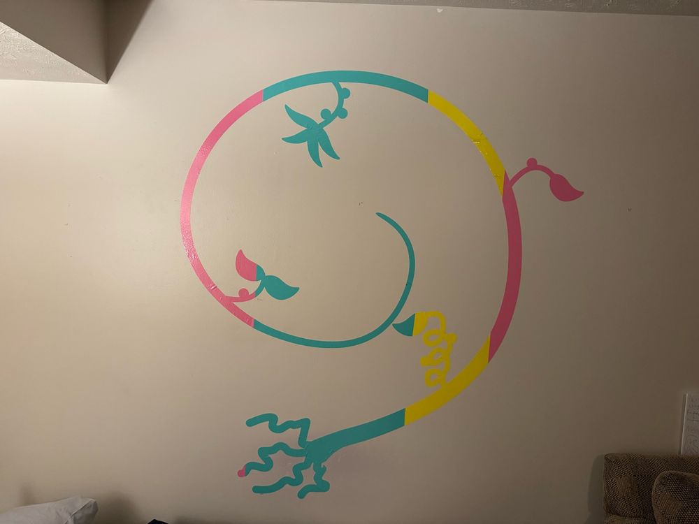 Large vinyl decal of a vine beginning with a root, leaves and berries throughout, divided into 4 color sections into pink, cyan, yellow, and pink. This is adhered to my bedroom wall