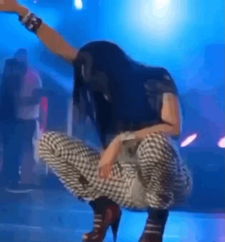 a woman in plaid pants and high heels squats on a stage