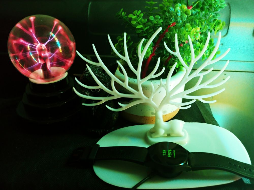 Deer with many antlers sitting over a charging smartwatch, a plasma orb and small fake plant in the background.