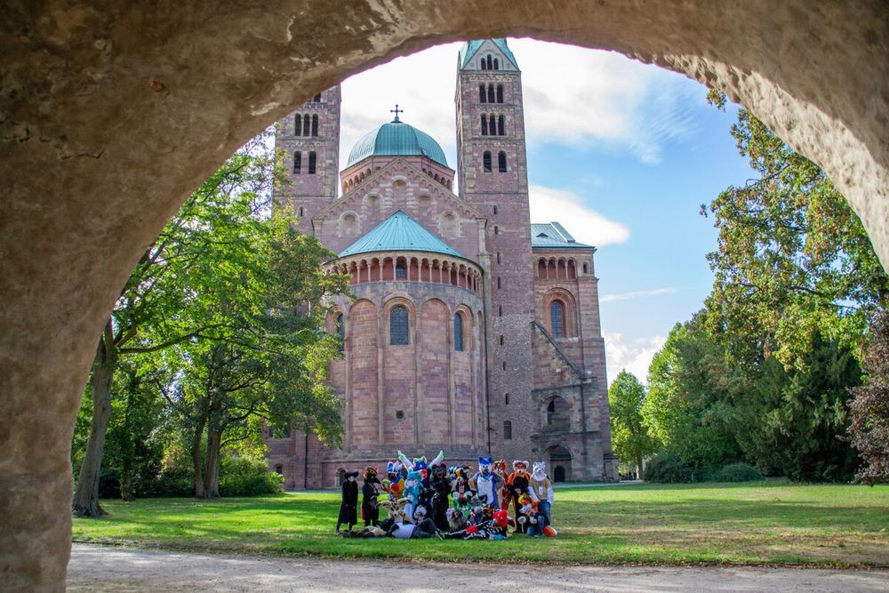 Fursuiter vor Schloss umringt von Bäumen, Torbogen im Vordergrund