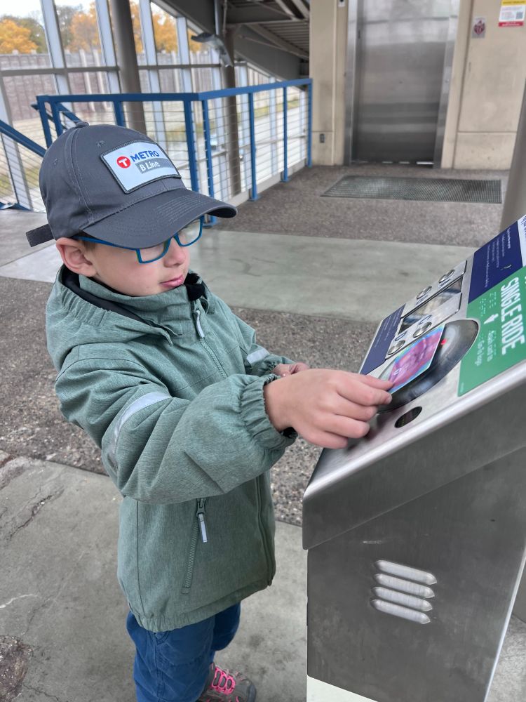 6-year-old wearing a B Line hat and tapping a “Ride with Pride” go-to card at a fare card validator at 35W & 46th Street station 