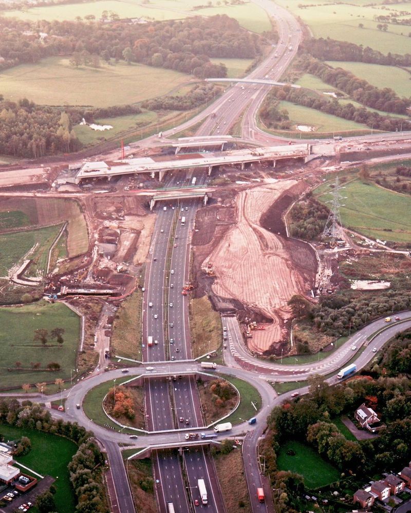 Aerial photograph of a motorway with a junction in the foreground and another much bigger multi-level junction being built in the distance